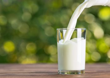 milk from jug pouring into glass on wooden table outdoors
