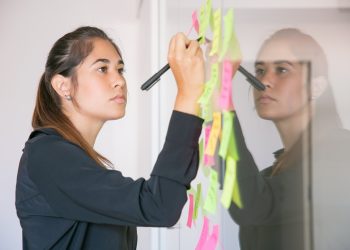 Young Latin businesswoman writing on sticker with marker. Focused confident beautiful brunette female manager sharing idea for project and making note. Brainstorming, business and training concept