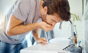 Man in bathroom, brushing teeth and rinse with water, morning cleaning routine for health and wellness in home. Dental care, mouthwash and toothbrush, male grooming for fresh breath and oral hygiene.
