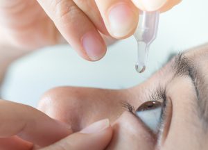 Close up view of young asian woman applying eye drop to left eye, artificial tears.